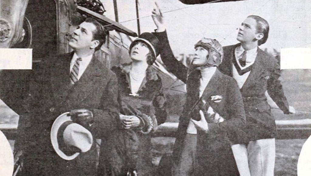 Four people standing next to an aircraft, looking up